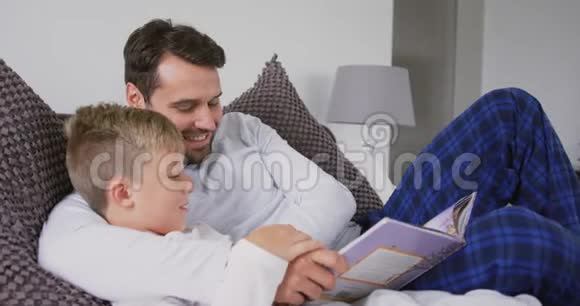 父亲和儿子在卧室的床上读故事书视频的预览图