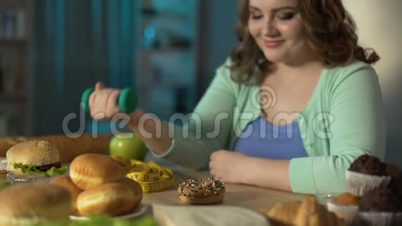 体重超标的女孩举起小哑铃傻笑地看着甜甜圈节食视频的预览图