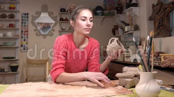 一般的看法一个女孩陶匠选择一个适当的流苏以微调生粘土杯在陶器车间视频的预览图