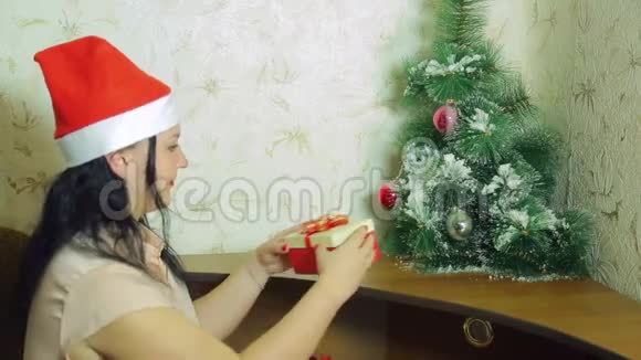 一个戴圣诞老人帽子的女人正在圣诞树下放圣诞礼物视频的预览图
