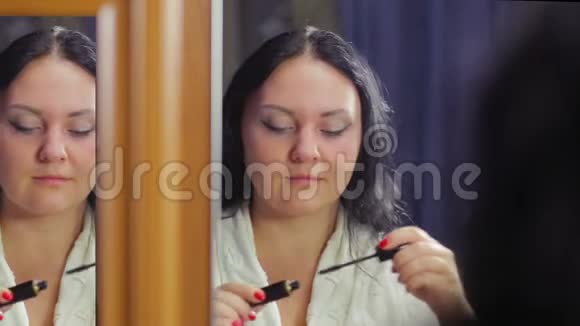 一个穿着白大褂的年轻女子在镜子前用睫毛膏涂睫毛视频的预览图