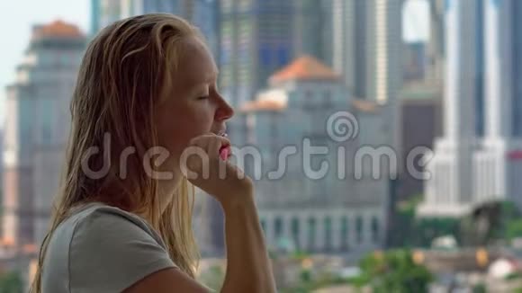 年轻女子刷牙站在阳台上可以看到一座城市中心的摩天大楼视频的预览图