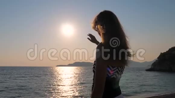 愉悦的女性双手捕捉天空中的太阳站在海岸上慢动作视频的预览图