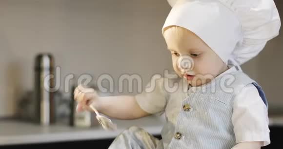 一个甜的小厨师在一个白色的烹饪帽混合面粉与金属勺子视频的预览图