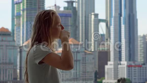 年轻女子刷牙站在阳台上可以看到一座城市中心的摩天大楼视频的预览图