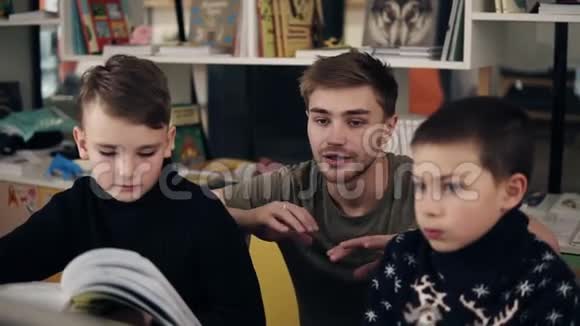 一个年轻迷人的男教师在一个节目中向两个小男孩解释一些事情的慢镜头视频的预览图