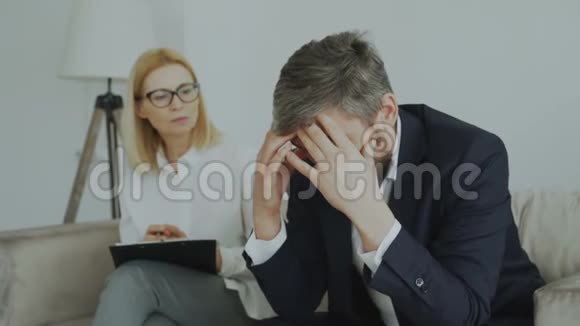 愤怒的哭泣的商人病人用双手抱着他的头在她的办公室里和他的精神分析师交谈视频的预览图
