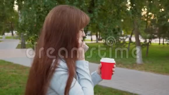 女商人戴着浅色西装眼镜在公园里散步喝咖啡在智能手机上聊天视频的预览图