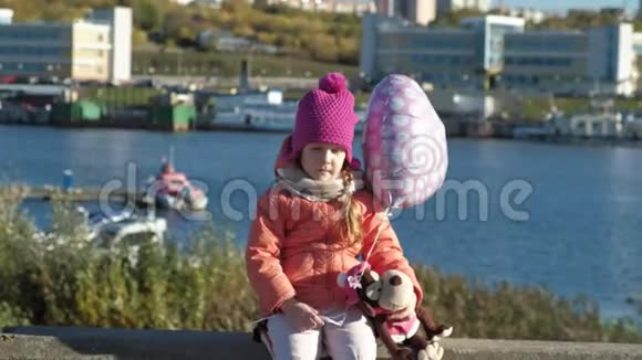 小女孩带着气球坐在河港上一边旅行一边微笑视频的预览图