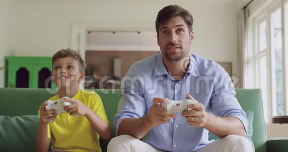 父子俩在家沙发上一起玩电子游戏视频的预览图