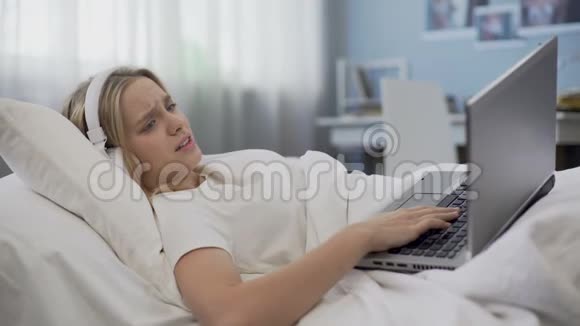 坐在社交网络上交流耳机的少女心烦意乱躺在床上视频的预览图