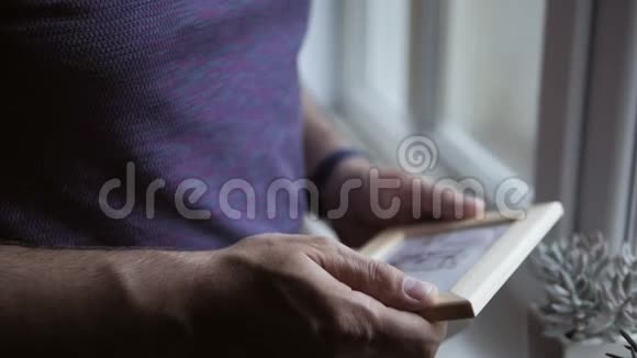 一个孤独的人站在窗前拿着一张木框里的照片人检查照片视频的预览图
