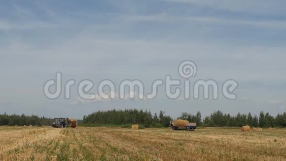 农夫一辆拖拉机拖着干草堆把一捆捆干草装进农场附近的拖车里视频的预览图