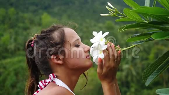 年轻美女的肖像触摸和嗅闻山上弗兰吉帕尼花的气味慢动作视频的预览图