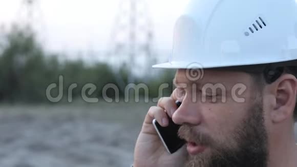 站技术负责人戴着白色安全帽站在电站附近与工人通电话视频的预览图