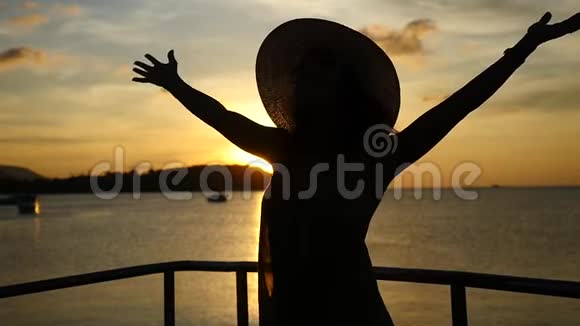 戴帽子的年轻女子伸出双臂在令人惊叹的日落时旋转泰国的海上游轮慢动作视频的预览图
