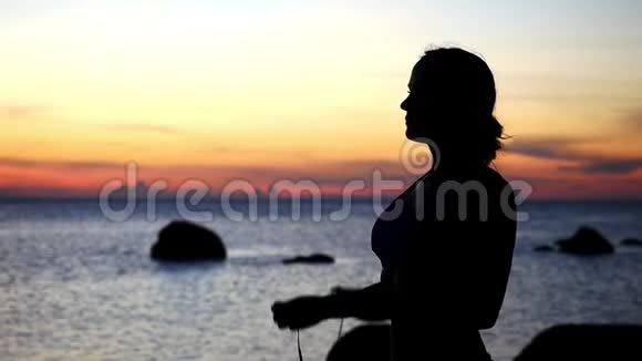 运动的年轻女子在海滩上跑步前戴着耳机欣赏日落动作缓慢1920x1080视频的预览图