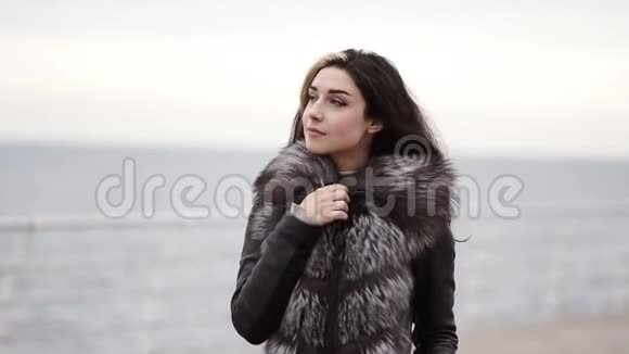 一位年轻的黑发女子穿着毛皮大衣在冬天走在海边或海洋上的肖像她越来越近了视频的预览图