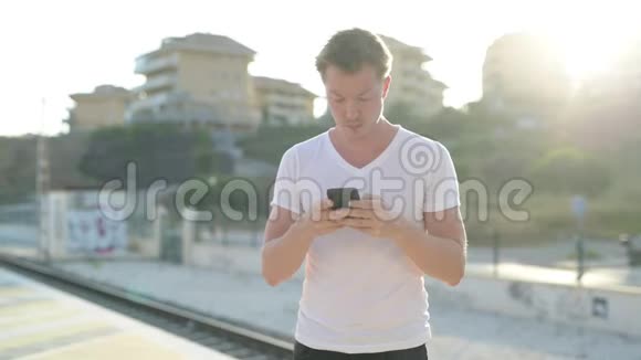 年轻的快乐游客在等待火车时使用电话视频的预览图