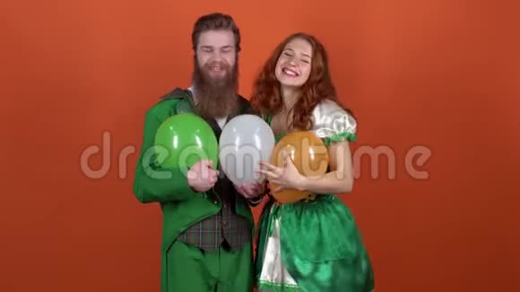 穿着圣诞服装的年轻夫妇庆祝圣帕特里克节他们被隔离在橙色的墙上扔气球视频的预览图