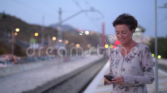 快乐成熟的旅游妇女在等待火车时使用电话视频的预览图