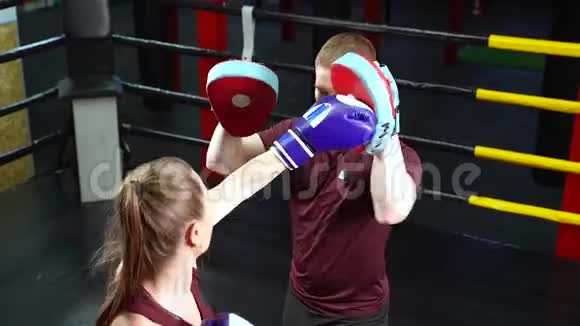 男性拳击教练在训练拳击场中的年轻女子时使用拳击脚垫视频的预览图