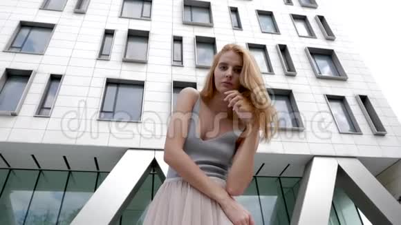夏天红头发的女人对着镜头对着背景模糊的公司大楼摆姿势视频的预览图