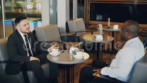 两个多种族的商人在午餐时间坐着微笑着在空中咖啡馆讨论他们的创业非洲视频的预览图