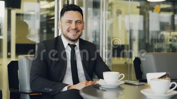 戴着正式服装坐着喝着咖啡在玻璃咖啡馆里微笑的快乐胡子白人商人的肖像视频的预览图