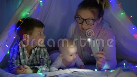 为人父母妈妈拿着一部手电筒的手机在wigwam为儿子读书视频的预览图