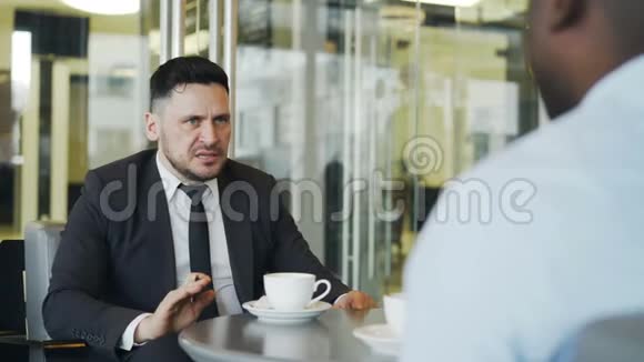 自信的白人商人在现代咖啡馆里给他的非裔美国人经理布置商务任务视频的预览图