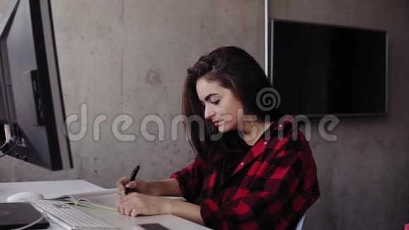 年轻漂亮的穿着红法兰绒衬衫的女孩在笔记本上写下了一些东西视频的预览图