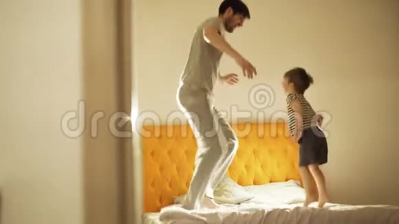 快乐的父亲和小儿子跳舞晚上睡觉前在家里的床上玩得开心视频的预览图