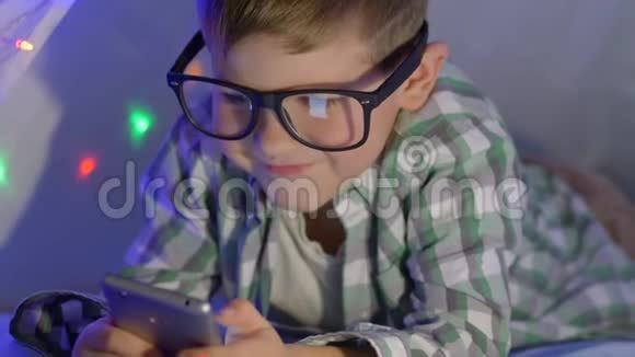 戴眼镜的小孩在家里用戴花环的wigwam看手机录像视频的预览图