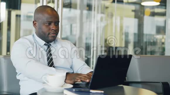 非裔美国商人在午休时间在玻璃咖啡馆思考打印和工作笔记本电脑他是视频的预览图