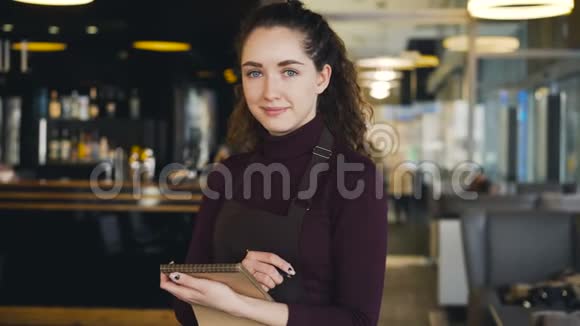活泼美丽的年轻女服务员站着留着菜单在狡猾的咖啡馆里真诚地微笑视频的预览图