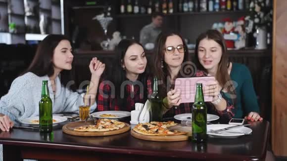 在一家有披萨和啤酒的餐馆里的朋友的陪伴玩得开心分享在平板电脑上观看照片视频的预览图
