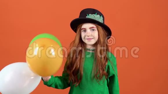 一个年轻的女孩拿着三个气球在橙色的墙上庆祝圣帕特里克节视频的预览图