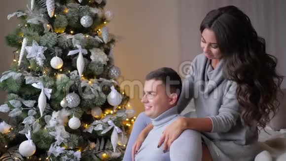 浪漫的时刻女孩坐在沙发上在圣诞节前夕拥抱丈夫靠近杉树视频的预览图