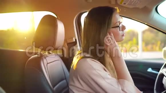 戴着眼镜的漂亮女孩把无线耳机插到耳朵里系好安全带就要开车走了视频的预览图