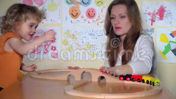 幼儿园保姆和好奇的小女孩玩木制玩具火车视频的预览图