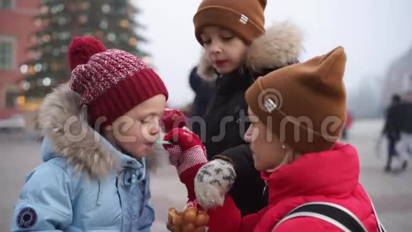 在圣诞树附近的广场上年轻的女人和两个男孩在吃气泡饼视频的预览图