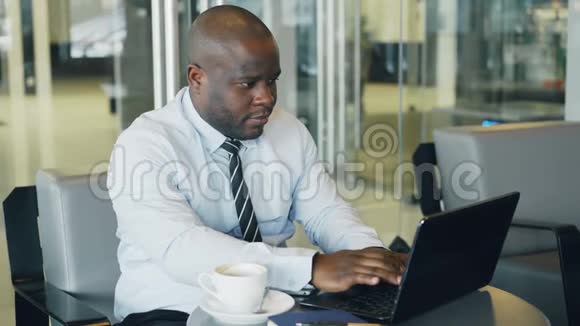 穿着正式服装的非裔美国商人看着他的笔记本电脑在时尚的咖啡馆里思考他的商业计划视频的预览图