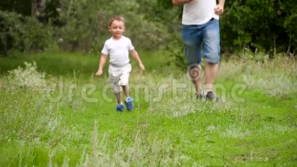 爸爸和宝宝在公园的绿草地里奔跑手牵着手慢悠悠的动作着视频的预览图