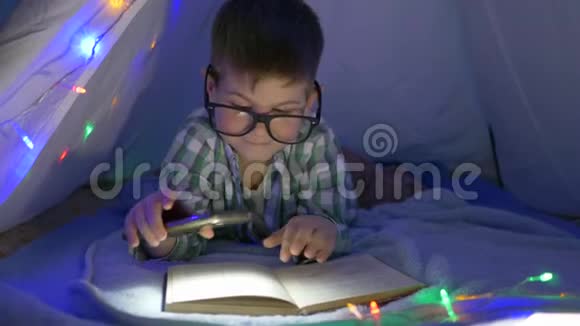 家庭教育戴眼镜的男孩手里拿着手电筒在帐篷里看书视频的预览图