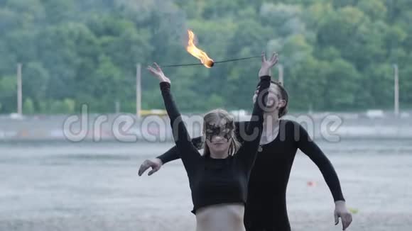 年轻漂亮的女孩和英俊的男人穿着黑色的衣服表演节目火焰站在河岸上那个女人视频的预览图