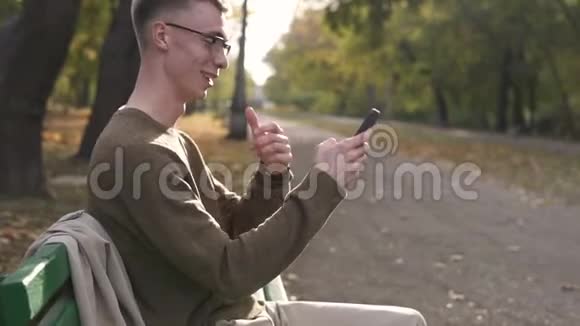 年轻的街头风格的男人喜欢在公园里使用他的智能手机年轻的白种人戴着眼镜视频的预览图