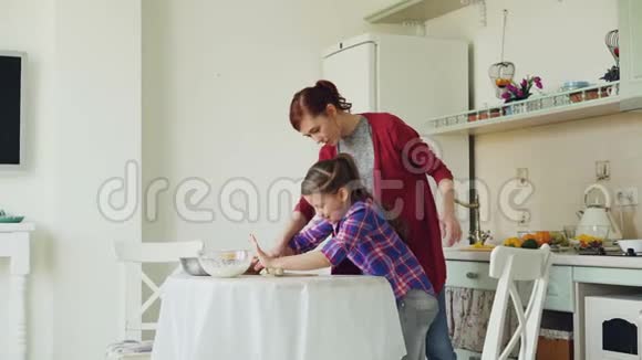 年轻的母亲教她可爱的小女儿在家里一起做饭时擀面团视频的预览图