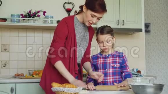 快乐的母亲教她可爱的小女儿在家里一起做饭时擀面团视频的预览图