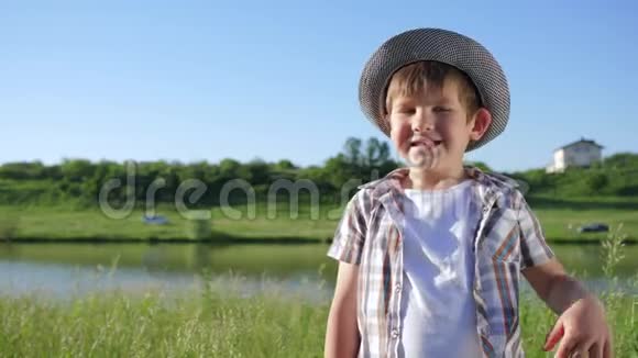 可爱的戴帽子的孩子在河边从大自然中的玻璃中喝水视频的预览图